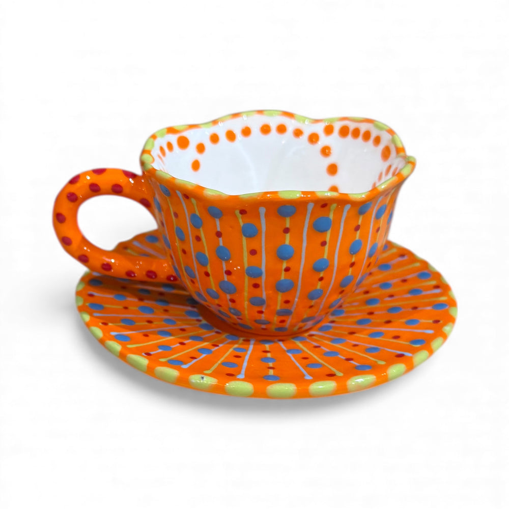 Polka dot teacup and saucer with orange, blue, and green pattern on a white background